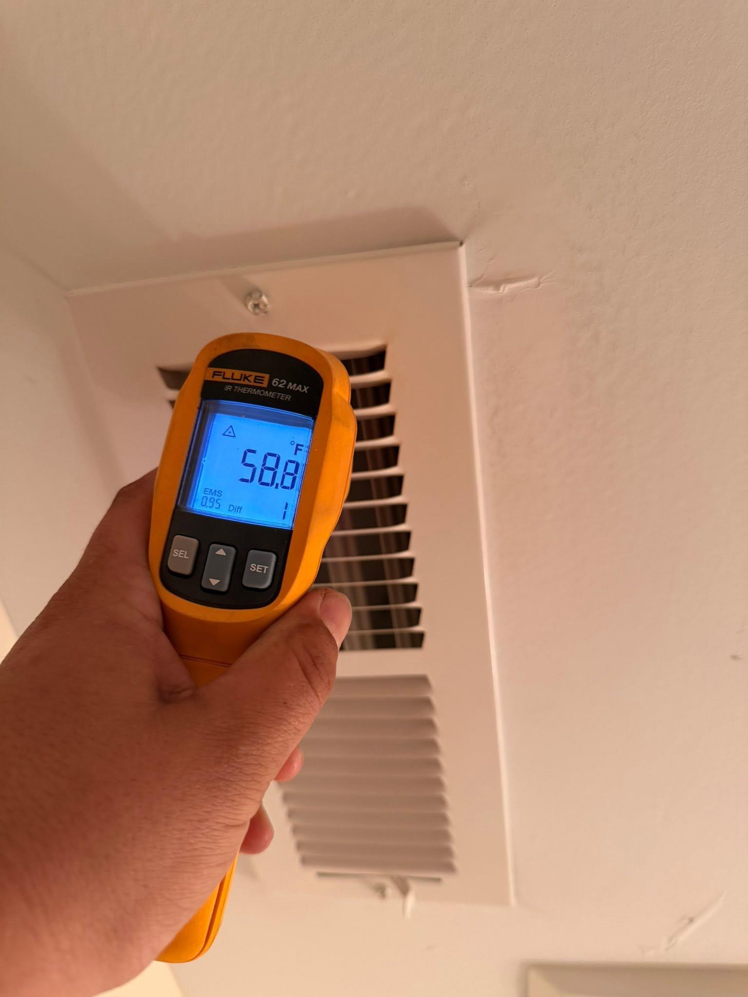 Technician checking supply-air temperature at an indoor HVAC vent