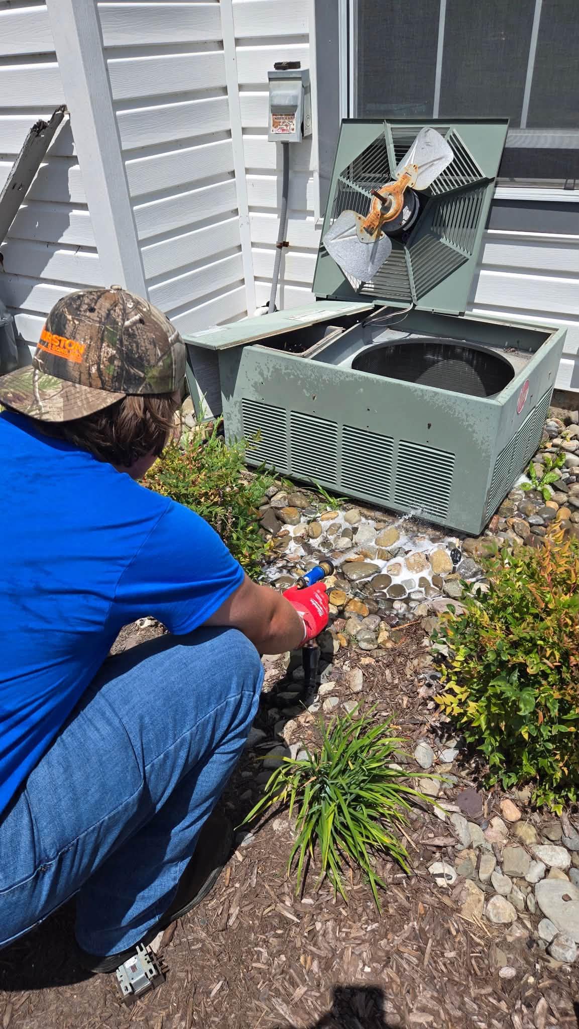 Ferguson & Sons technician cleaning an outdoor HVAC condenser during maintenance